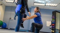 A physical therapist assists a patient using a harness support system in a rehabilitation gym.