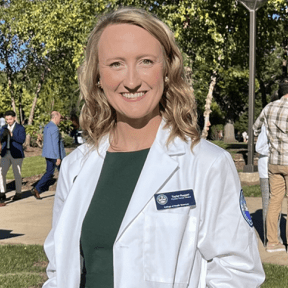 Student posing on campus in white coat