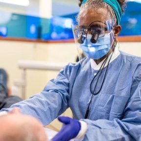 Dr. Johnson wears eye magnification, masks, and gloves while performing dental exam on male patient.