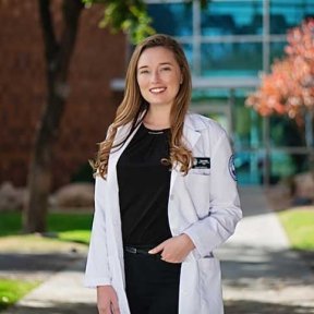 Student posing outside on campus in white coat