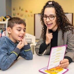 Speech-language pathologist reads out loud with young boy.