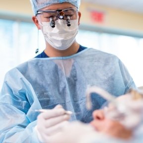 Dentist in protective gear using magnifying loupes while performing a procedure on a patient.