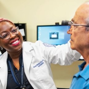Smiling healthcare provider examines an older patient in a clinic setting.
