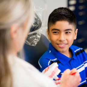 Smiling young boy sits in a dental chair while a dentist holds a dental model, explaining oral care during a checkup.