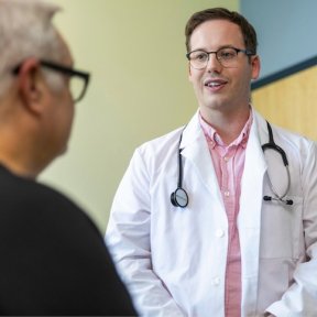 Two providers talk to patient in an exam room.