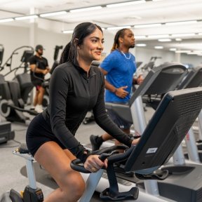 A woman on a stationary bike and a man on a treadmill exercise in a modern campus fitness center.