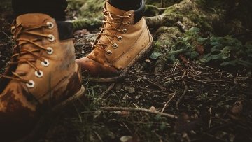 Person with muddy hiking boots walking in a forested area.