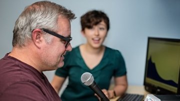 Man speaks into microphone while working with Speech-Language Pathologist.