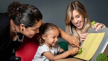 Child, alongside two speech language pathologists, pointing to picture