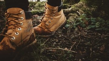 Person with muddy hiking boots walking in a forested area.