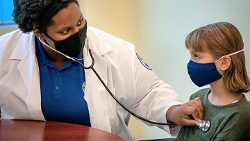 Doctor listening to child's heartbeat. Both are wearing masks.