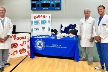 Dr. Durso, Dr. Williams, and dental student William Boensch in white coats in front of their booth at the Senior Fair in Lemont.