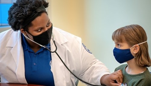 Doctor listening to child's heartbeat. Both are wearing masks.