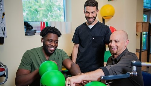 Occupational therapist gently holds male patient’s arm and guides him to manipulate green balls.