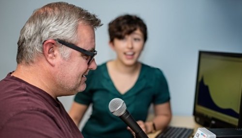 Man speaks into microphone while working with Speech-Language Pathologist.