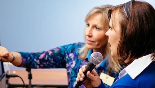 Woman speaks into a microphone with assistance from speech-language pathologist.