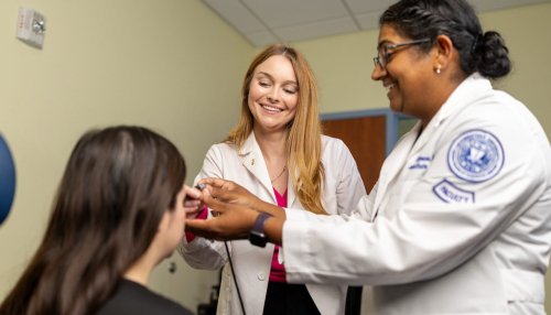 Two clinicians perform an eye examination on a patient in a clinical exam room.