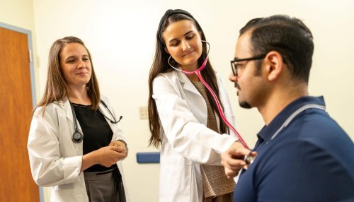 student checking heart rate of patient as doctor observes