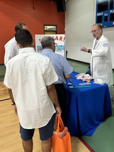 Dr. Durso in a white coat shares information at the booth with attendees standing in line. 